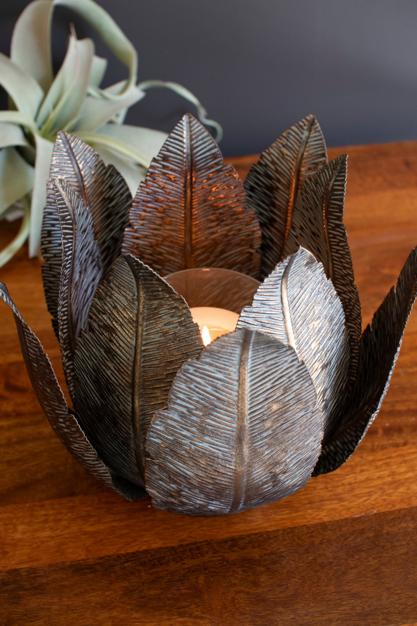 Antique Brass Metal Leaf Base with Glass Hurricane showcasing an elegant leaf silhouette surrounding a flickering candle.