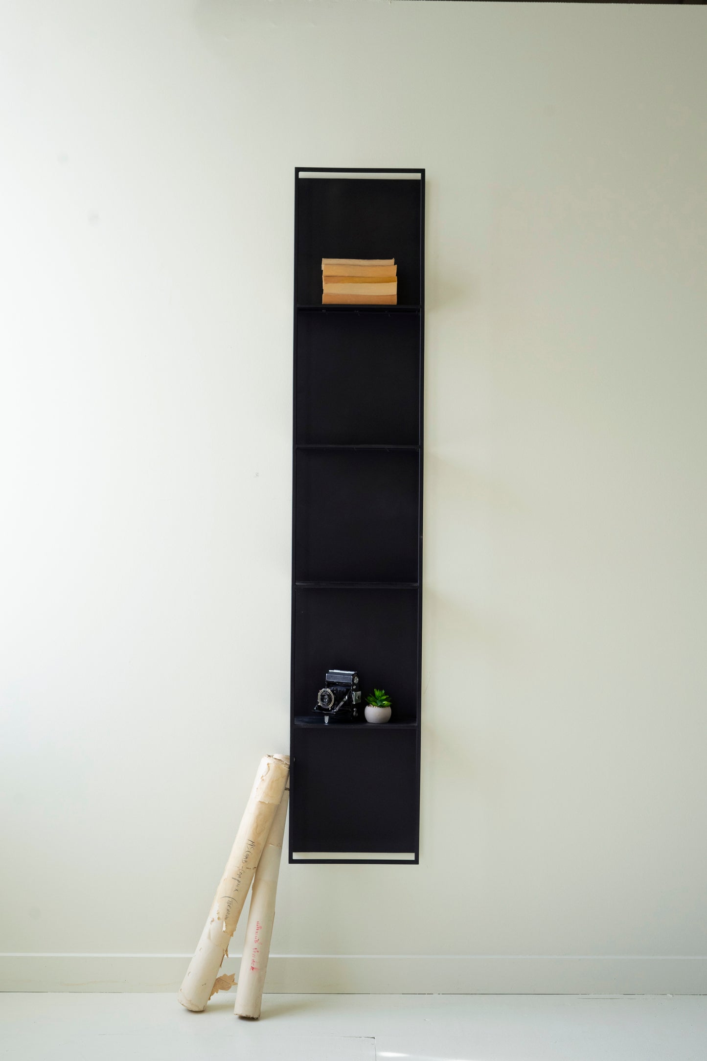 Black Metal Four-Tiered Wall Shelf displaying books and decor, mounted on a light wall with decorative items below.
