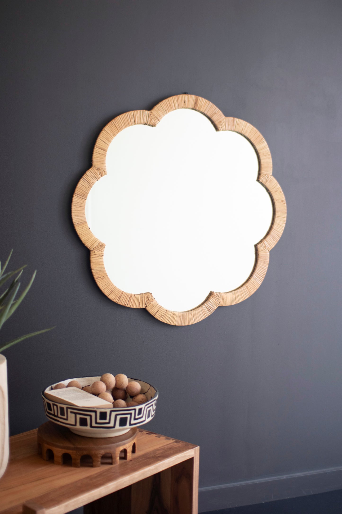 Cane Wrapped Flower Shaped Framed Mirror displayed on a dark wall, complementing decorative bowl and wooden shelf.