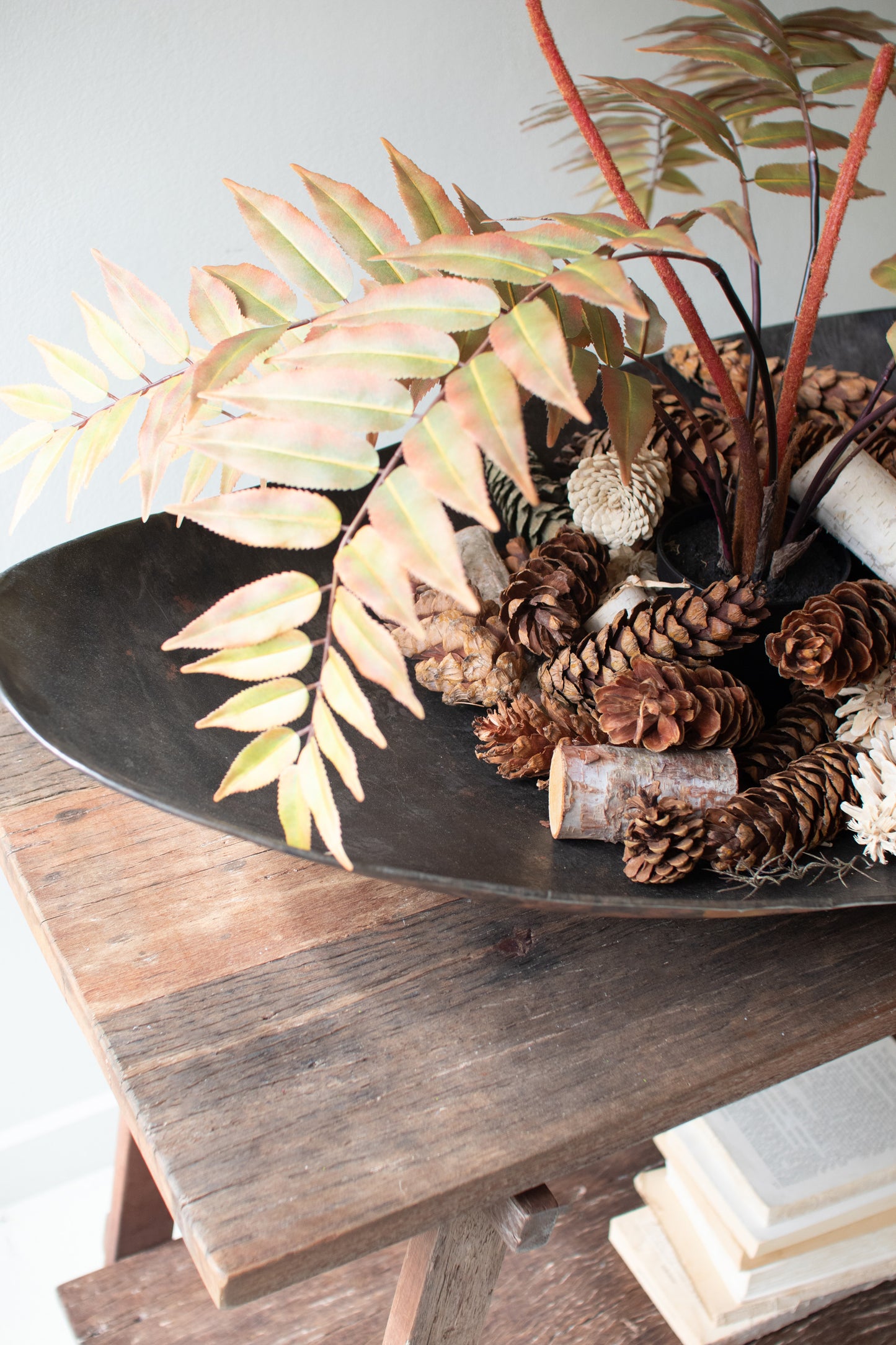 Giant Rustic Iron Oval Bowl filled with pinecones and foliage, beautifully displayed on a wooden table.