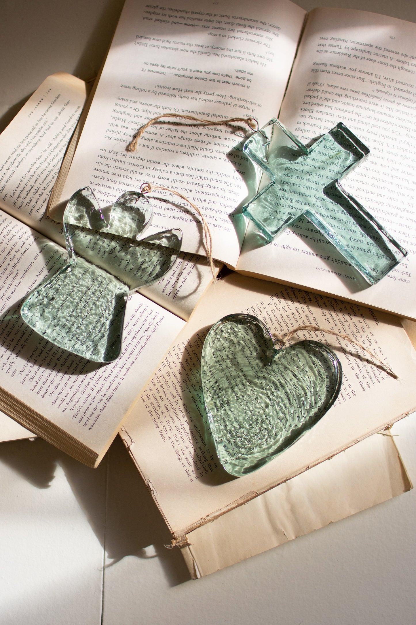 Glass Heart Suncatcher, angel, and cross suncatchers displayed on open books, showcasing their unique glass designs.