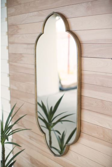 Decorative wall mirror with a gold frame on a wooden wall.