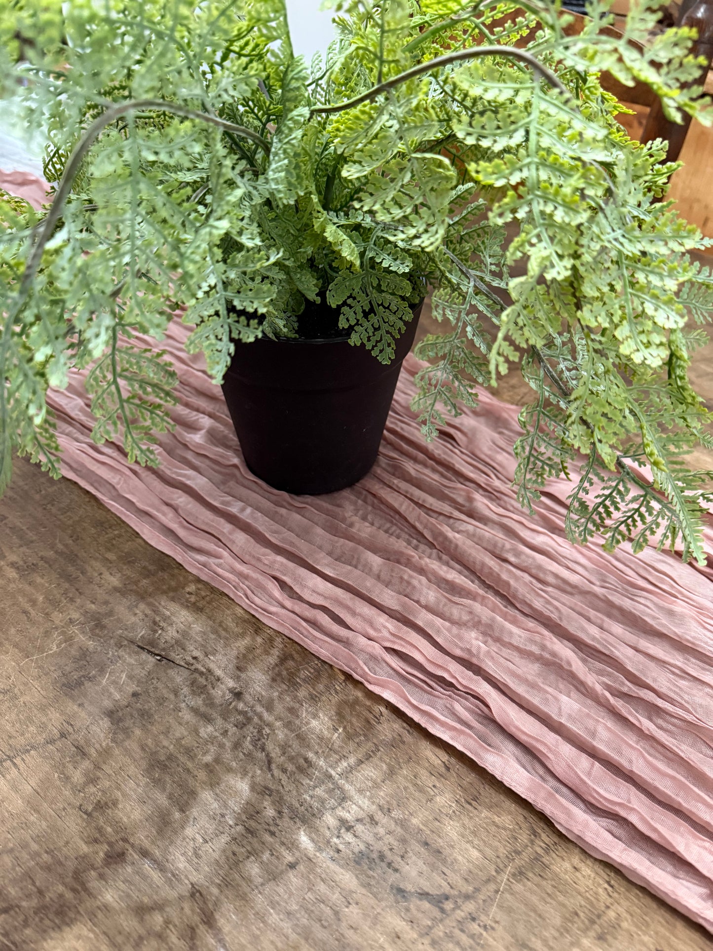 Pink Crinkle Fabric table runner with Fern plant on a wooden table
