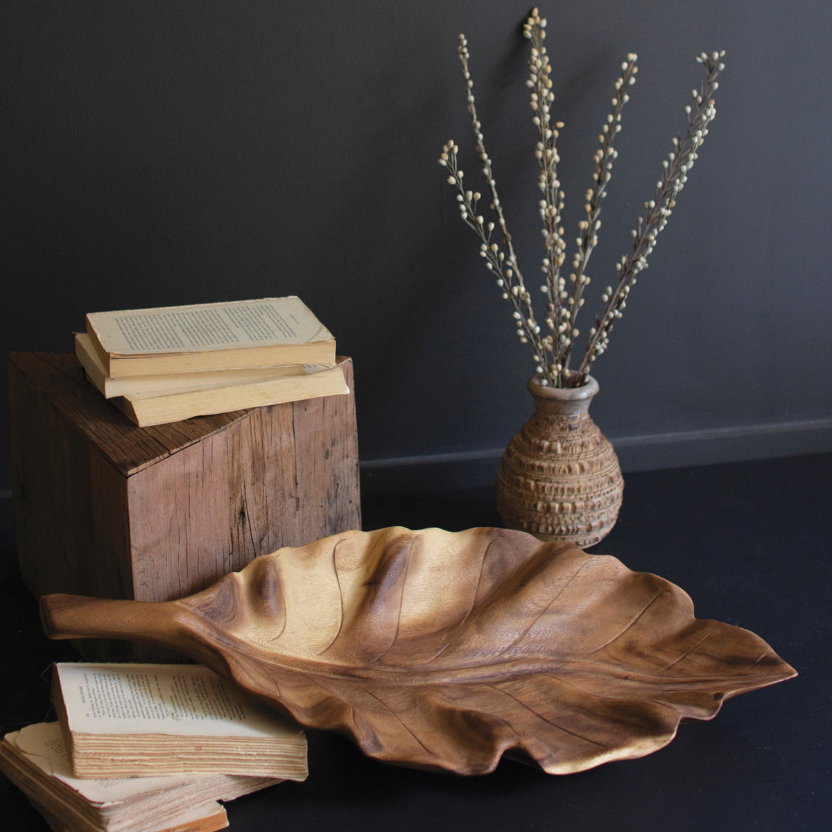 Teakwood Leaf Tray with organic leaf shape, placed beside books and a textured vase with dried flowers.