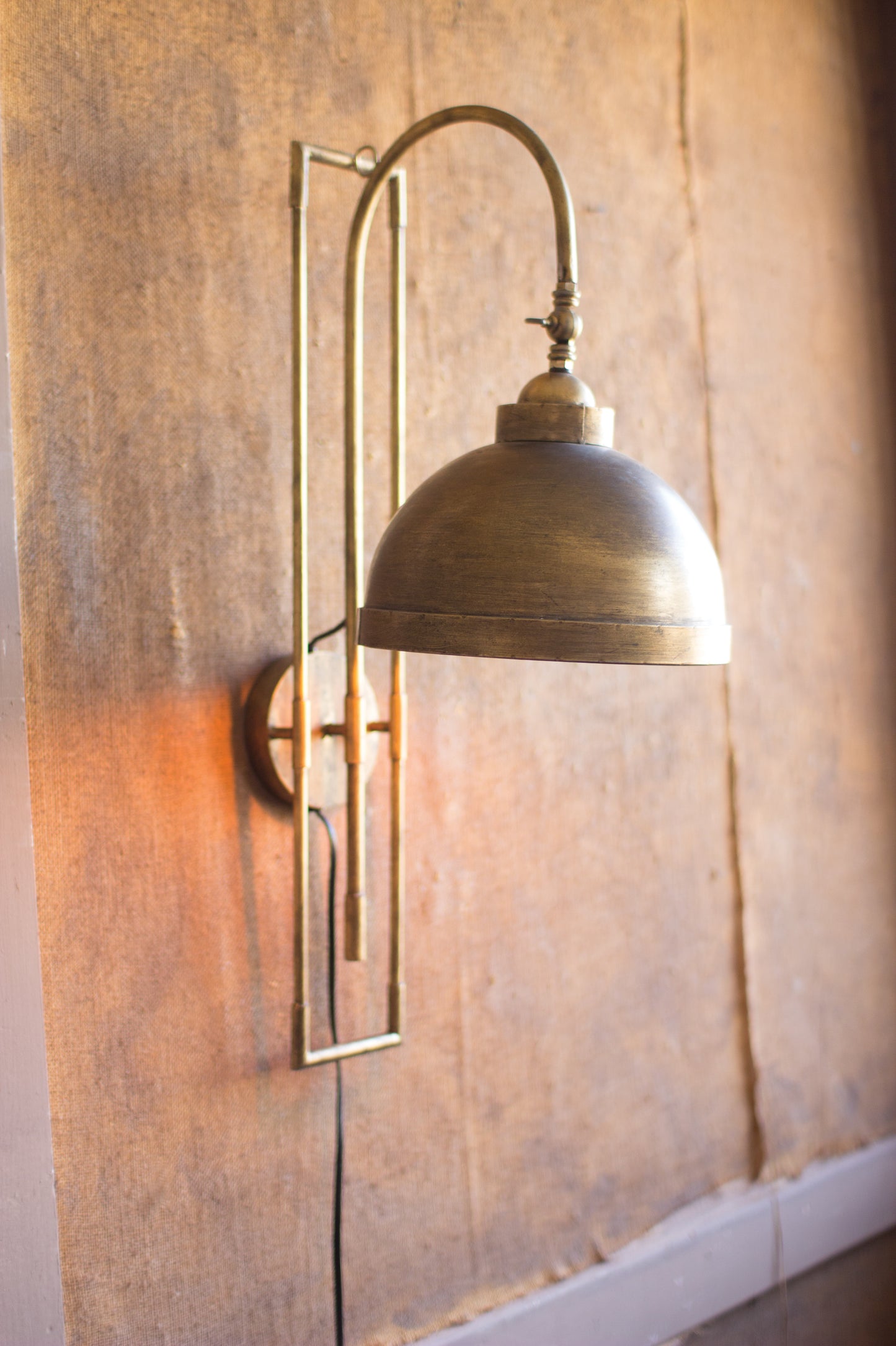 Antique Brass Metal Wall Sconce, featuring a rounded shade and a sleek, simple design against a textured wall.