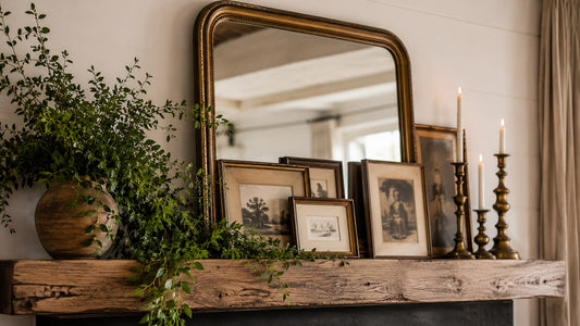 modern rustic mantel with vase of greenery, aged brass mirror and old framed photograph with brass candle holders and cream candles burning