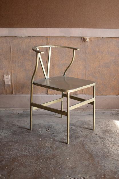 AntiqueBrassFinishMetalWishboneChair - Gold metal chair against a plain wall with concrete floor