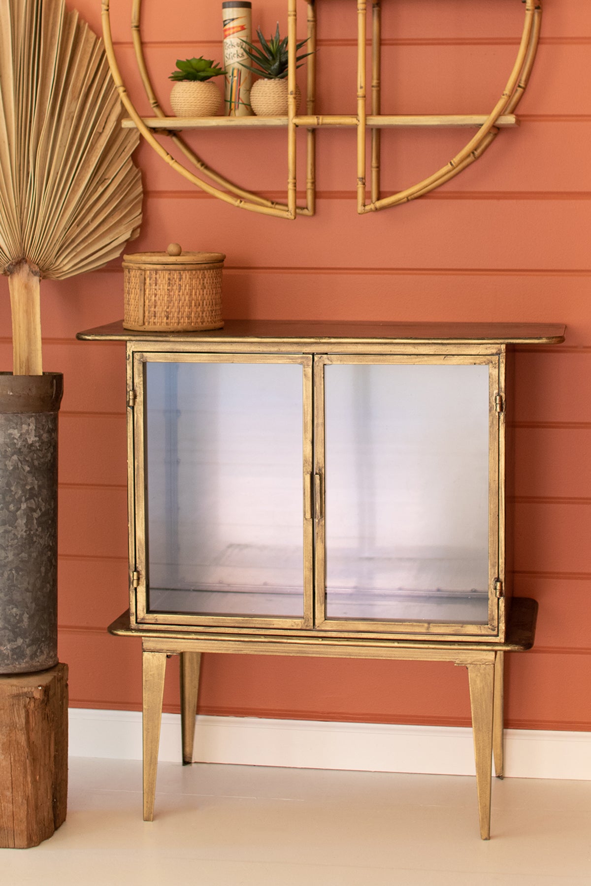 Antique brass cabinet with two glass doors against a red wall with decorative elements.