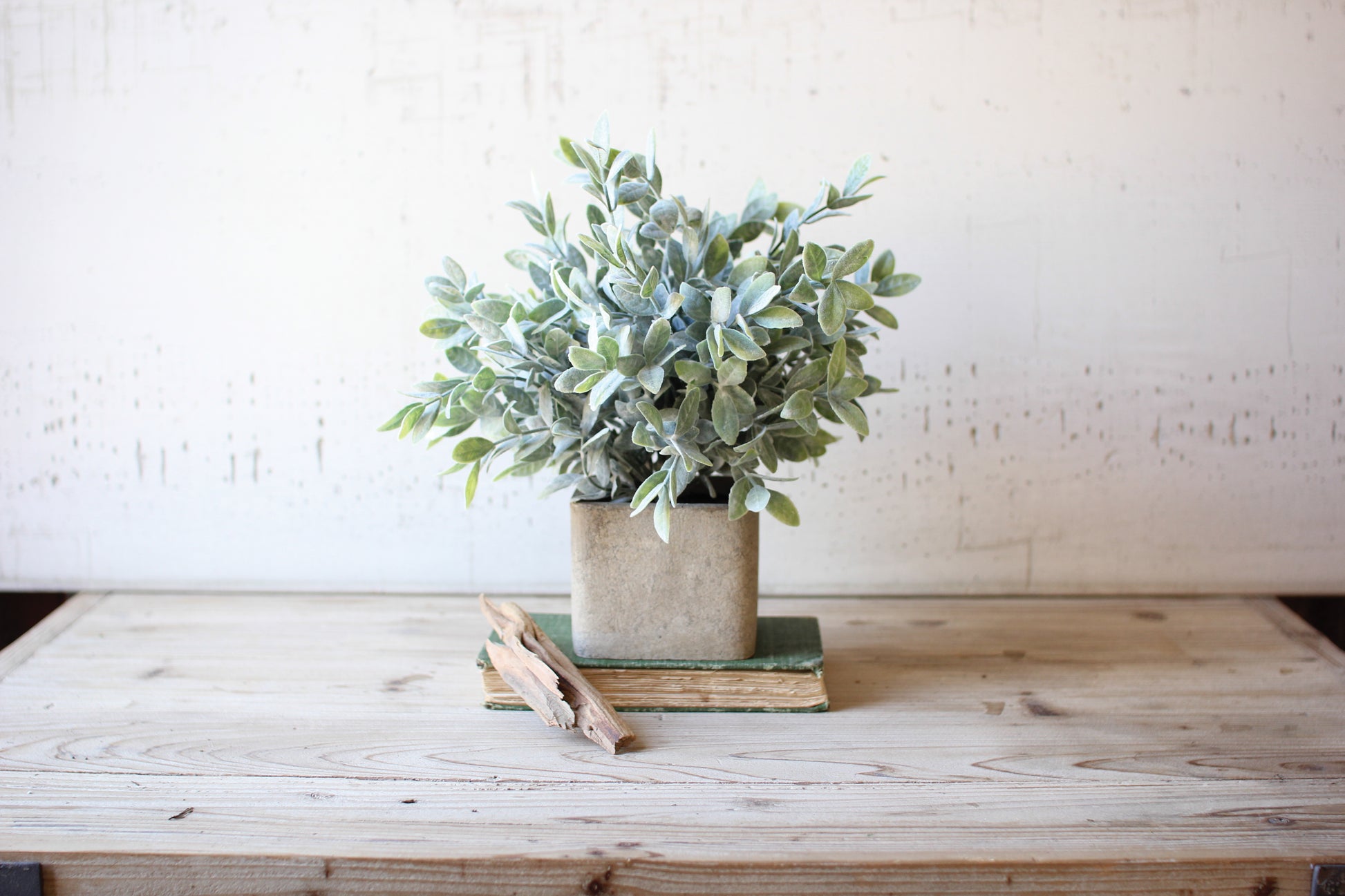 ArtificialSageBushInaSquarePot - faux greenery in a square pot atop book