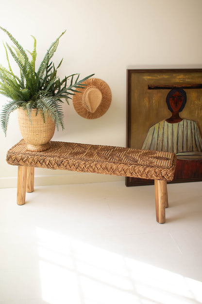 Banana Fiber and Teakwood Bench with hand-woven seat, natural plant, and art piece in background.