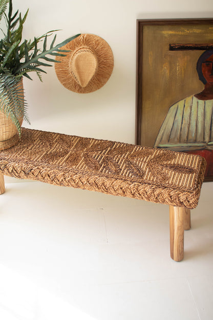Banana Fiber and Teakwood Bench with a hand-woven natural fiber seat and wooden legs, adorned with a plant and artwork.