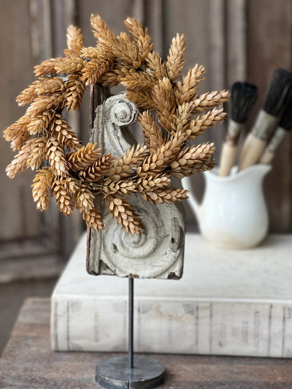 A beige hops candle ring with fall floral design, displayed on a table with a background of a workshop.