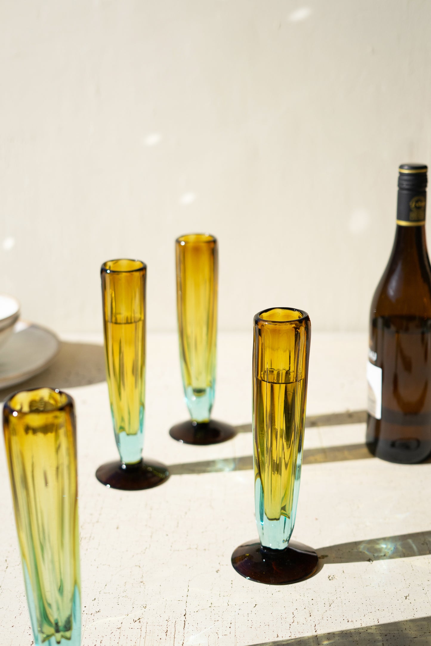 BlueandAmberRecycledChampagneGlass-2 - Set of colorful glass tumblers on a table with a bottle in the background.