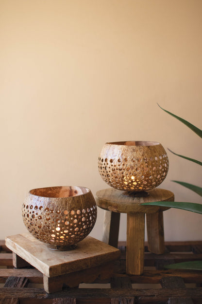 Carved Coconut Luminaries - Set of 2 on wooden stools, showcasing intricate hand-carved details and a warm, natural glow.