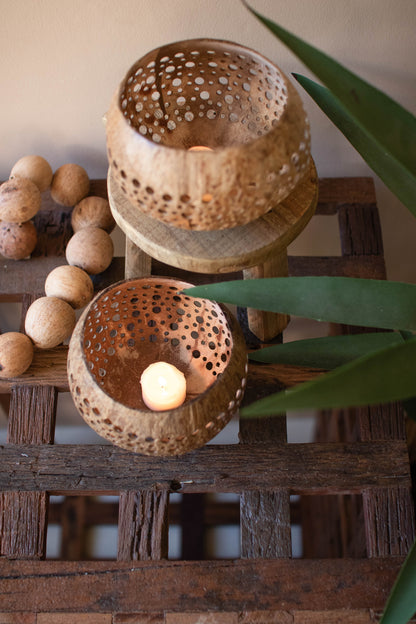 Carved Coconut Luminaries - Set of 2 displayed on a rustic wooden table with subtle candlelight glow.