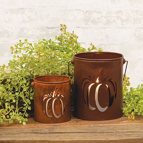 Two rust-colored metal candle holders with pumpkin designs on a wooden surface with green plants.