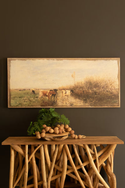 Field of Cows Painting on Burlap against a dark wall with a framed landscape painting.