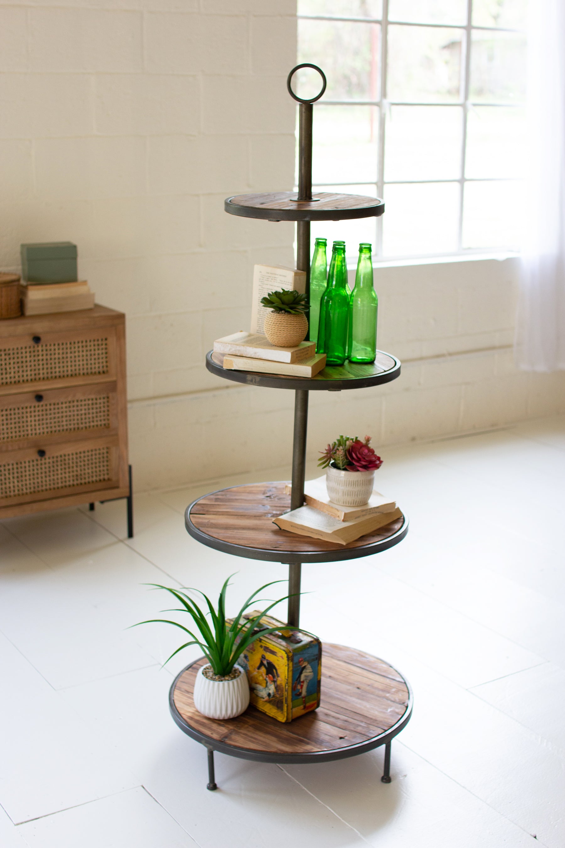 Four-tiered recycled wood and metal tower with decorative items in a room with a window and furniture.