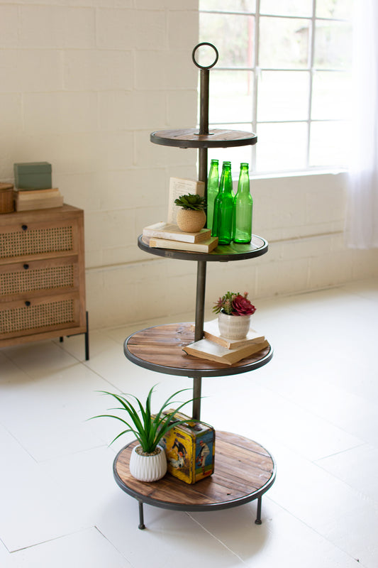 Four-tiered recycled wood and metal tower with decorative items in a room with a window and furniture.
