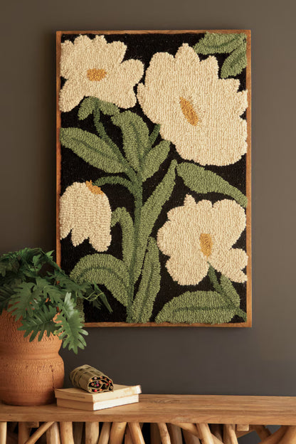 Framed Hand-Hooked Art with White Flowers beside potted plant.