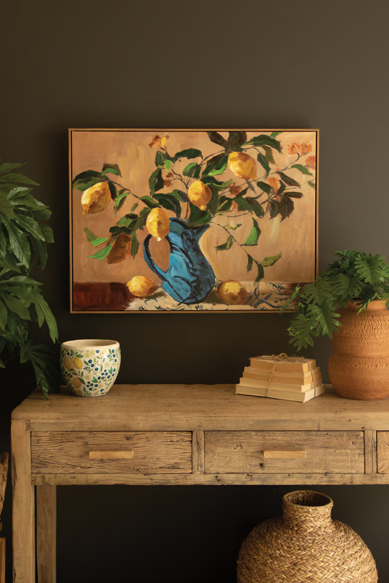 Framed Lemon Branches in a Blue Vase Painting and books on a wooden table against a dark wall.
