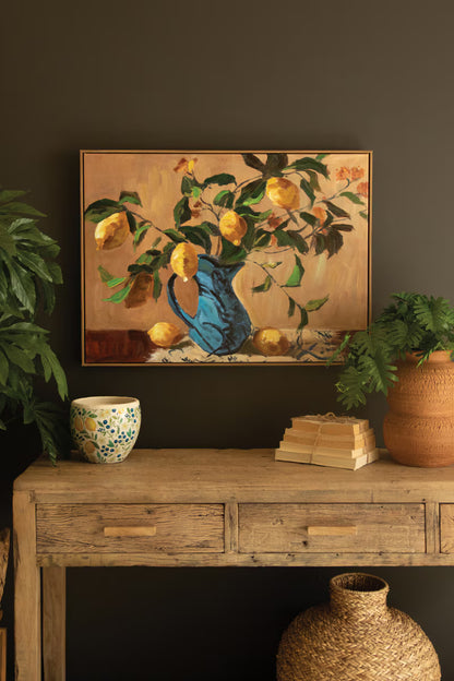 Framed Lemon Branches in a Blue Vase Painting and books on a wooden table against a dark wall.