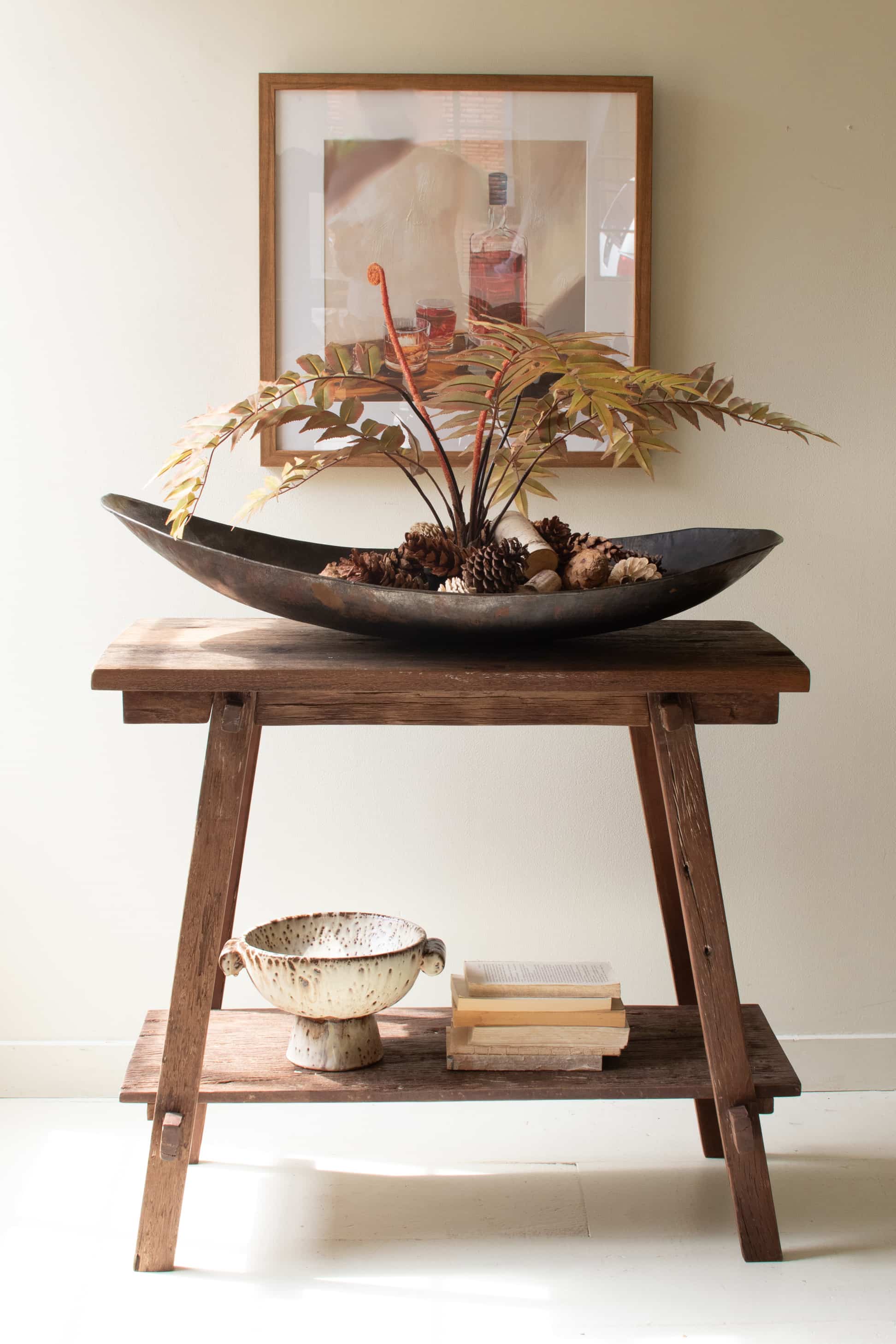 Wooden table with decorative items including a bowl with plants and a framed picture on the wall.