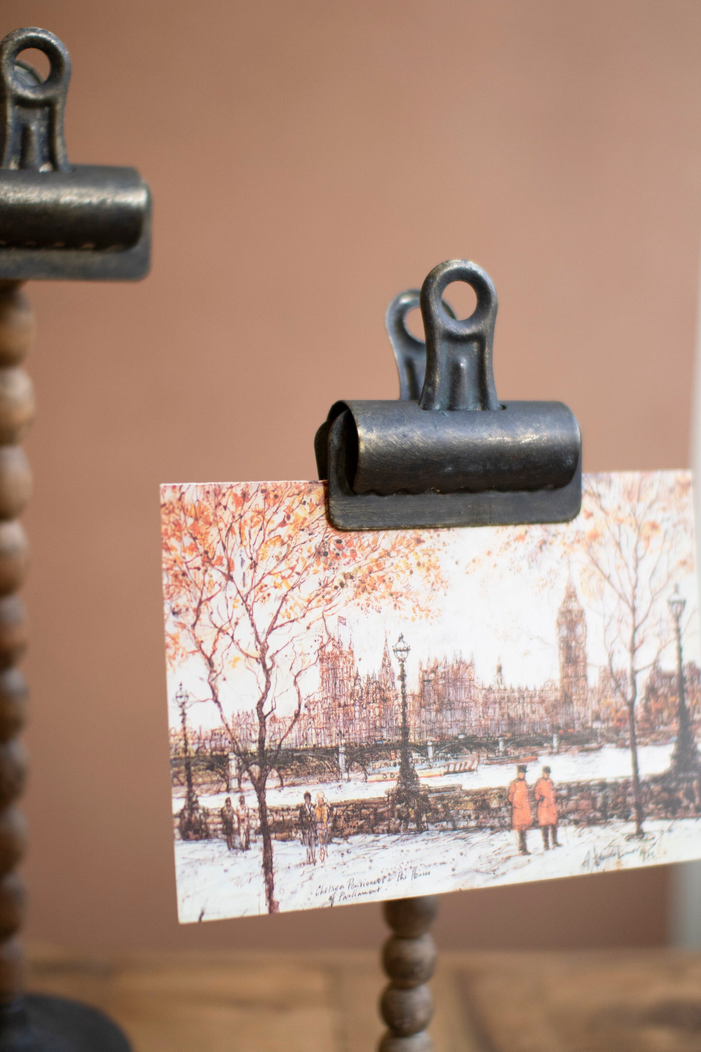 Metal Clip with Beaded Stem holding a postcard with a winter scene of a cityscape.