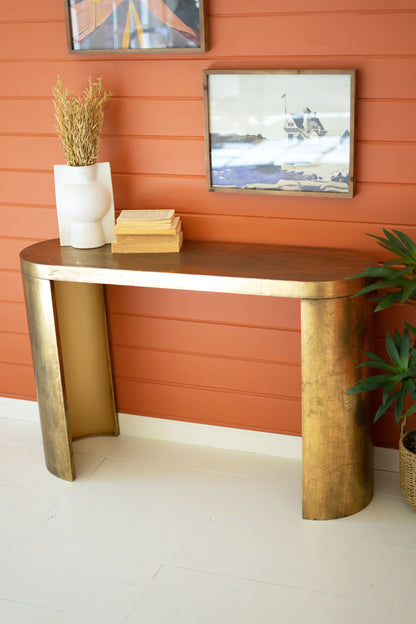 OvalAntiqueBrassEntrywayTable against an orange wall with decorative items.