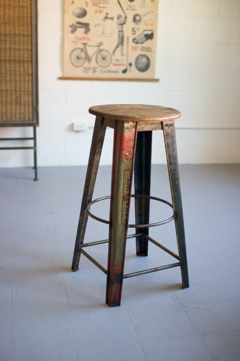 Vintage-style RecycledMetalBarStoolwithWoodenSeat in a room with a poster on the wall.