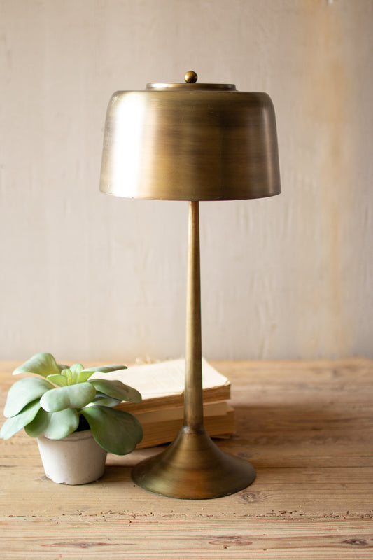 Tall Antique Brass Table Lamp with Brass Shade on a wooden surface with a plant and books in the background