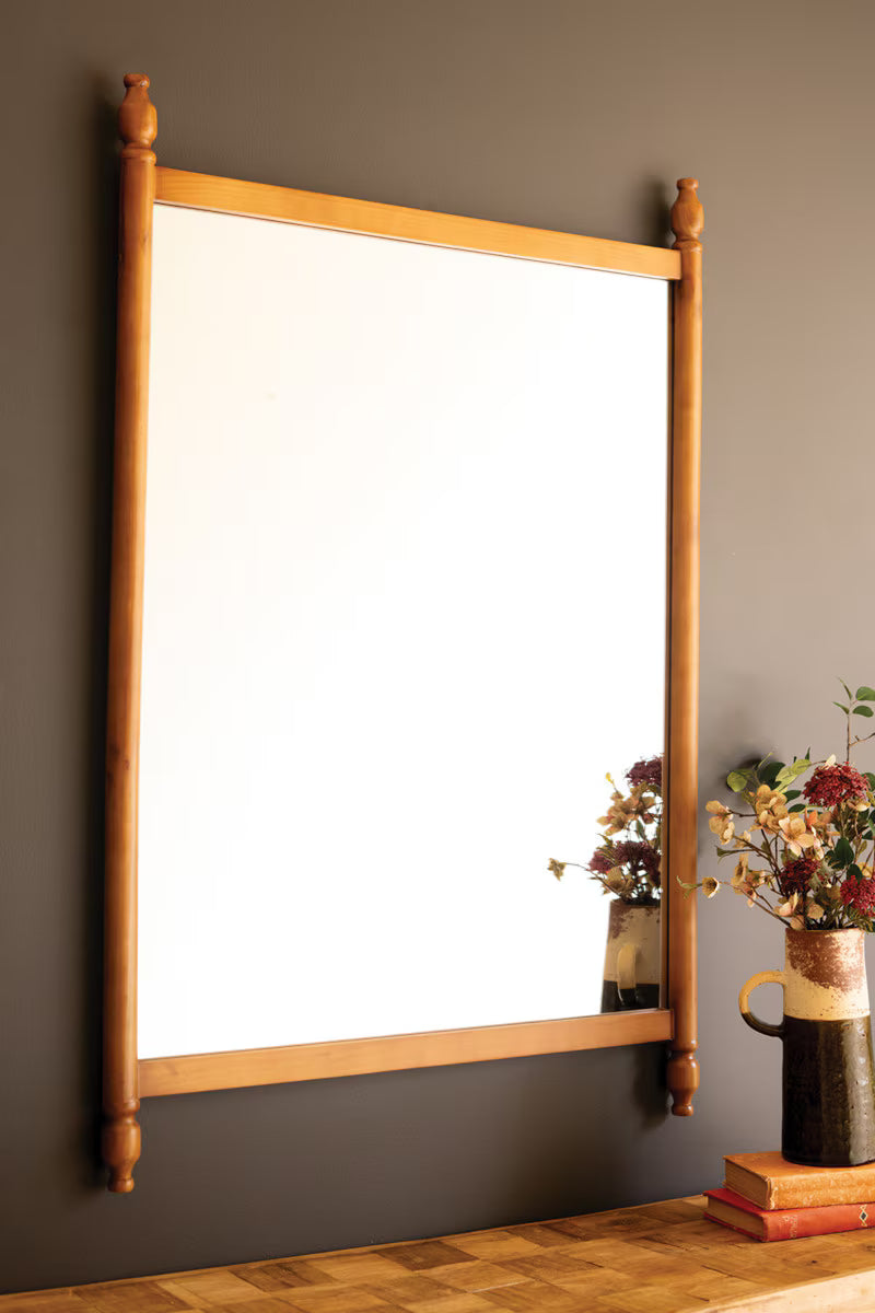 Wood Framed Mirror with Finials hanging on a dark gray wall above a wooden table. 