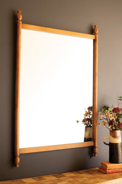 Wood Framed Mirror with Finials hanging on a dark gray wall above a wooden table. 