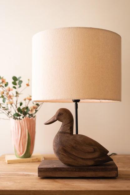 Wooden Duck Table Lamp with a beige lampshade on a wooden surface.