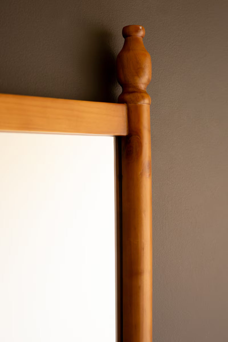 Wooden Mirror with Finial against a dark brown wall.