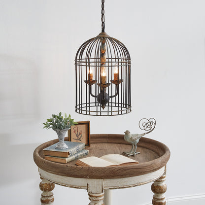 A rustic bird cage pendant light with a metal cage design hanging over a wooden table with a decorative item and books on it.