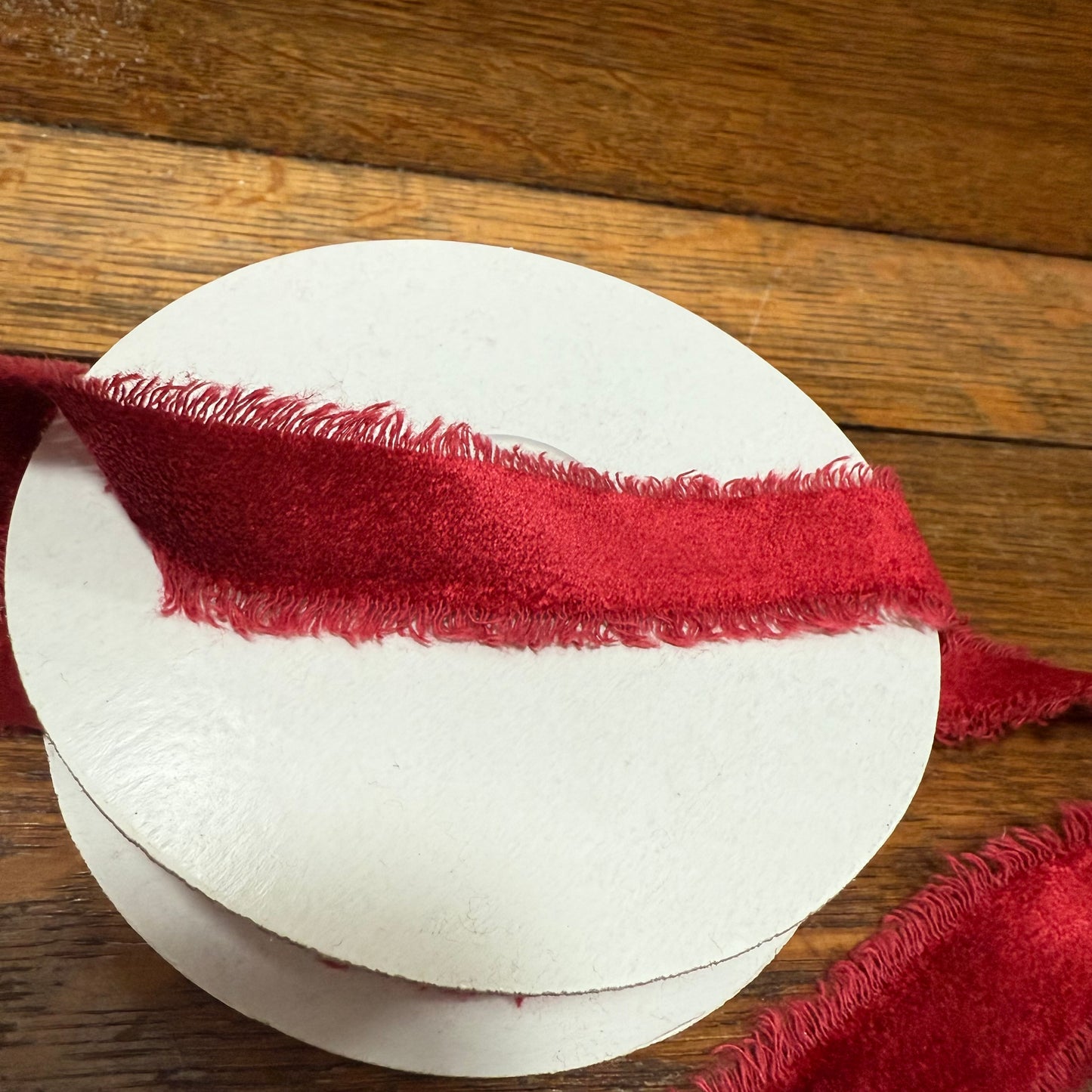 burgundy red ribbon on a spool of white thread against a wooden background