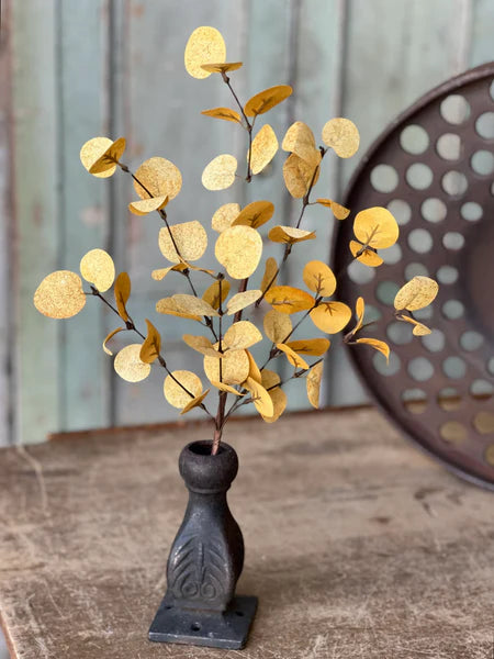 Decorative fall plant with yellow leaves in a black vase on a wooden surface.