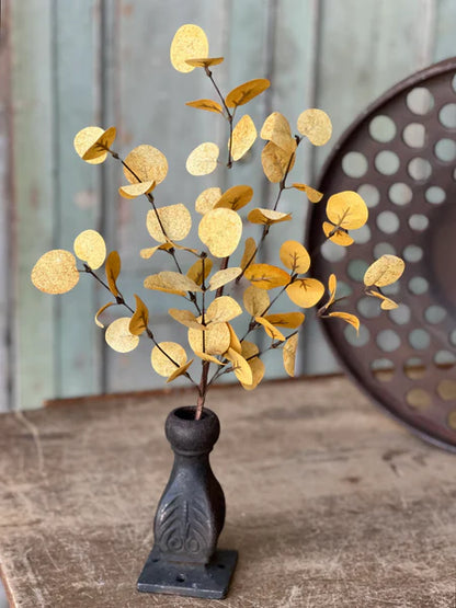 Decorative fall plant with yellow leaves in a black vase on a wooden surface.