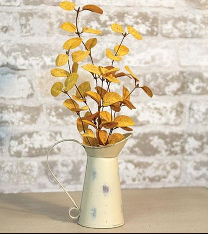 Vintage-style white watering can with yellow leaves against a textured white wall.