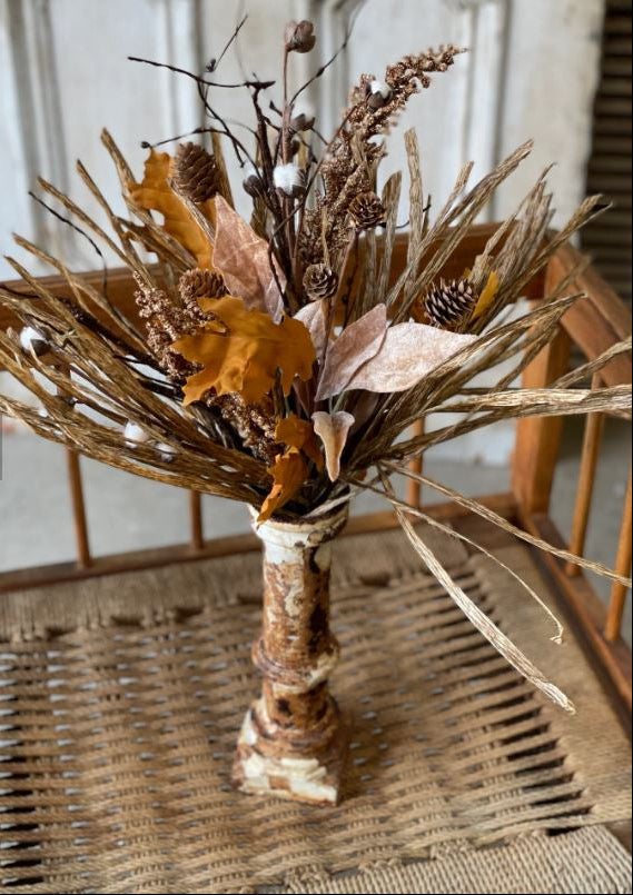 A dried floral arrangement featuring a variety of fall-colored materials such as faux cotton, pine cones, and artificial leaves on a printed raffia base.