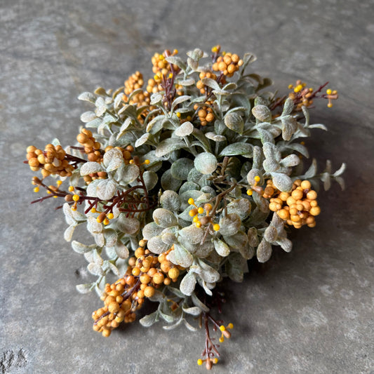 A cluster of artificial floral stems featuring dusty sage-green leaves and small round golden-yellow berries, arranged on a textured gray stone surface.