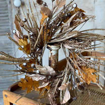 A fall wreath decorated with faux cotton, pine cones, bubble berry shoots, and fall leaves on a printed raffia paper base, displayed on a wooden object.