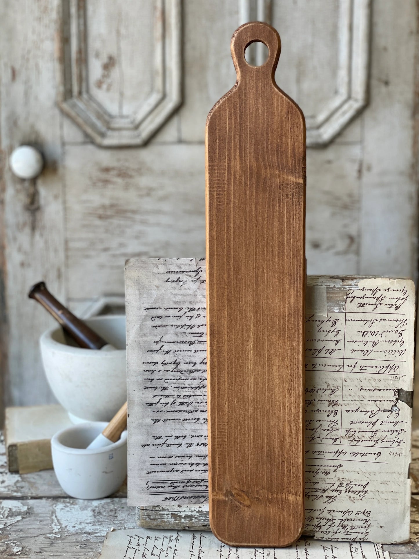 A large wooden layering plank placed on a rustic wooden surface with a blurred background containing kitchen items.