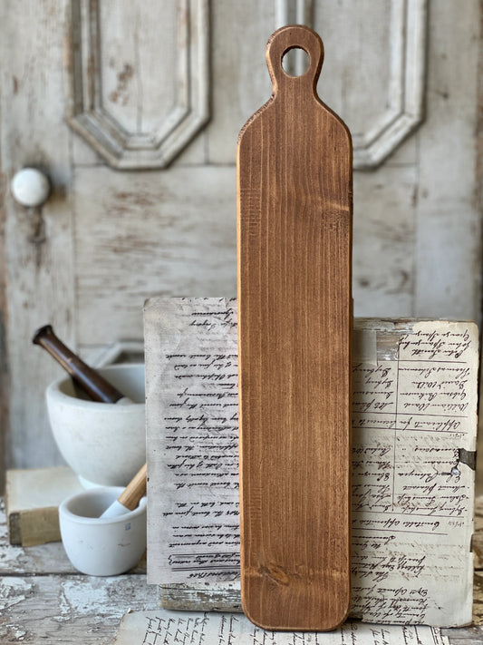 A large wooden layering plank placed on a rustic wooden surface with a blurred background containing kitchen items.