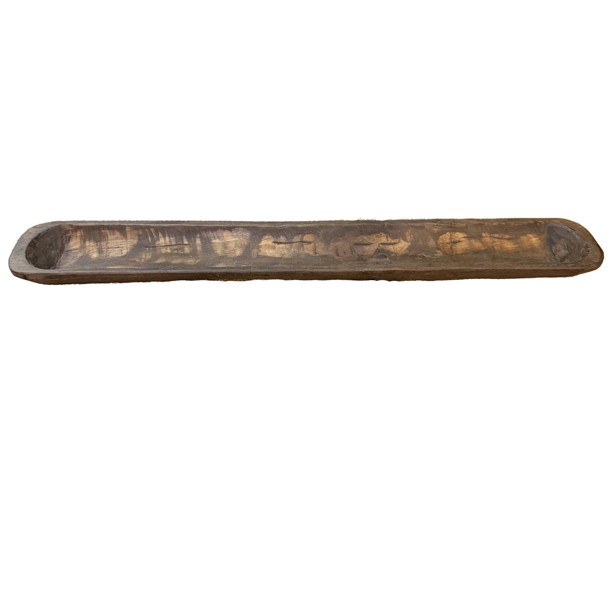 A long, narrow rustic wooden bowl with a dark brown finish and visible grain, displayed on a patterned runner.