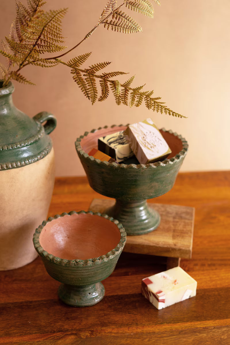 Two green ceramic bowls on a wooden surface with a vase and leaves in the background.