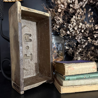 Vintage wooden box engraved, next to stacked books and dried plants.