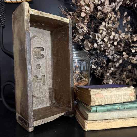 Vintage wooden box engraved, next to stacked books and dried plants.