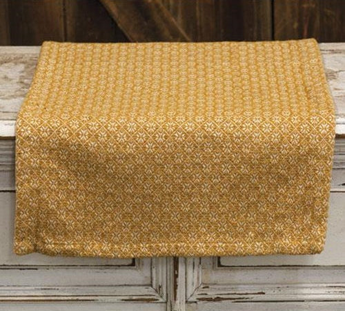 A rectangular table runner with a textured mustard yellow and white geometric pattern, draped over a rustic white wooden table.